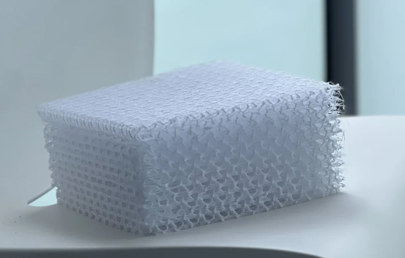 A textured white sponge sits on a modern white chair with soft lighting and a blurred background, conveying a minimalistic and clean tone.